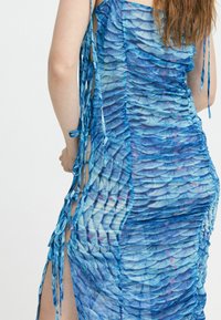 Blaues Raffungskleid mit einem strukturierten Design, das Schuppen ähnelt, seitlichen Ausschnitten und Bändern, die verstellbare Öffnungen für eine taillierte Silhouette schaffen.