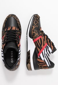 Baskets présentant un mélange de motifs léopard et zèbre en marron, noir et blanc, avec des accents rouges et un col noir texturé.