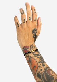 Bracciale di pelle con hardware dorato su un polso tatuato; i tatuaggi visibili includono una rosa e vari motivi grafici.