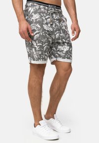 Pantalones cortos grises con un estampado blanco de hojas, con cintura elástica y dobladillos enrollados. Combinados con zapatillas blancas.