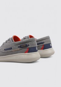 Zapatos de tela gris con textura de algodón, forro naranja contrastante, acentos azul marino, ojales de metal y suela de goma beige claro.