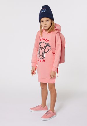 Abito felpa rosa con grafica di elefante e testo "KENZO PARIS", abbinato a sneakers rosa. Uno zaino rosa abbinato e un berretto blu navy completano il look.