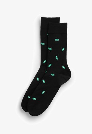 Černé ponožky do šatníku s vzorem malých zelených ikon dolaru rozptýlených po látce.