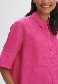 Camicia a maniche corte, con bottoni, realizzata in lino rosa. Presenta un colletto e due tasche anteriori. Tessuto morbido con un design dalla vestibilità rilassata.