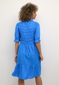 Rochie albastră cu un bust elastic, mâneci scurte și fustă învoltată. Fabricată dintr-un material fin, dispune de o croială lejeră și un tiv de lungime medie.