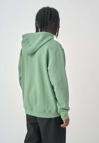 Green hoodie made of soft fabric, featuring a large hood, ribbed cuffs, and hem. The design is simple with no noticeable patterns or accents.
