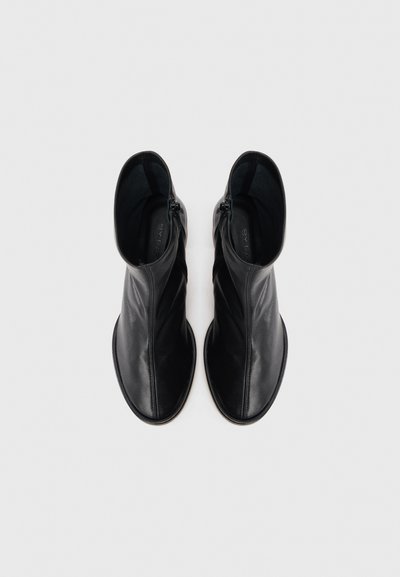 Schwarze Leder-Stiefeletten mit glatter Textur, ausgestattet mit einem seitlichen Reißverschluss und einem minimalistischen Design. Rund geschlossene Zehen und gepolsterter Innenraum.