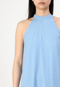Light blue halter neck top with textured dot pattern, featuring a fitted collar and loose fit, made from soft, smooth fabric.