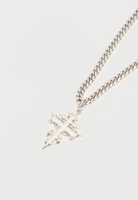 Ezüst nyaklánc vastag láncszemekkel és díszes medállal, mely keresztmintát ábrázol, részletes görbületekkel és éles csúcsokkal.