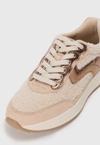 Helebeige tennisjalad pehme ja tekstureeritud pealisega, metallik pronksaktsentidega ja lame beige paeltega. Pehmendusega vahejäik ja ümar varvas.