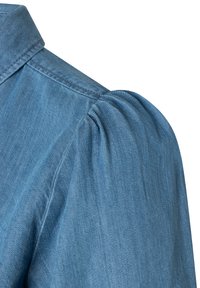 Spalla di camicia di denim blu con dettaglio di manica a sbuffo arricciata e cuciture visibili sul colletto e sulla cucitura.