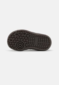 Braune Gummisohle mit einem strukturierten Traktionsmuster, das kreisförmige und sechseckige Vertiefungen aufweist, sowie dem eingeprägten "adidas"-Logo.