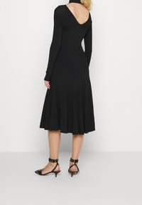 Svart långärmad klänning med V-rygg, ribbad textur, utsvängd kjol och figurnära liv. Matchad med svarta stilettklackar med nitar.