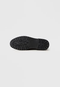 Suela de bota negra con un patrón de relieve profundo y diseño de reloj de números romanos embellecido en el centro.