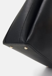 Borsa a tracolla in pelle nera con una forma geometrica, caratterizzata da accenti in hardware dorato alla base e dettagli di cucitura visibili.