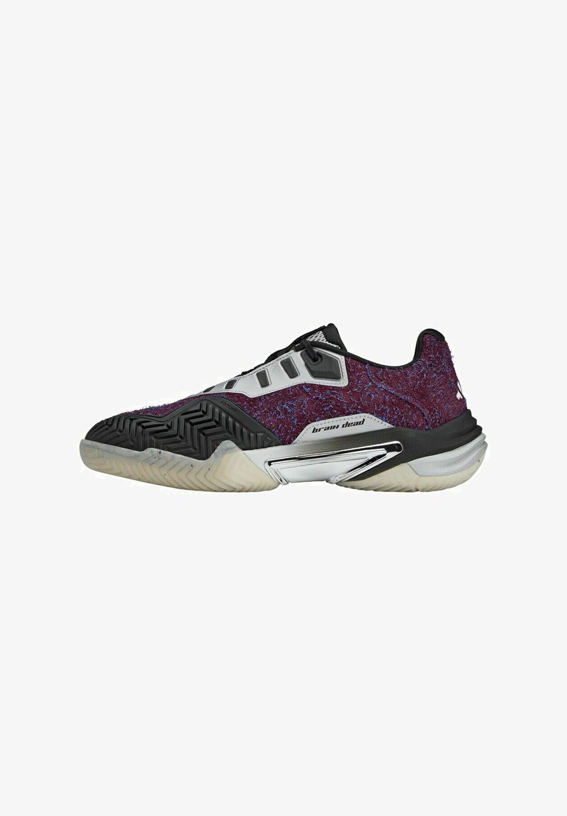 Scarpe da tennis con una tomaia texture viola, dettagli neri e una suola in gomma con un motivo a zigzag per una maggiore aderenza. Dettaglio del marchio in argento visibile.