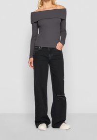 Off-shoulder långärmad topp i mörkgrått tyg, tillsammans med svarta vida jeans med slitna detaljer och vita sneakers.