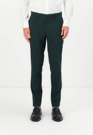 Mörkgröna skräddarsydda byxor i slät väv, med slim fit och rak framsida, kombinerat med svarta skor och grå strumpor.