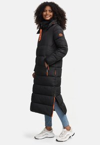 Long black puffer coat with orange accents, zippered pockets, and hood. Features quilted texture and side slits for ease of movement.