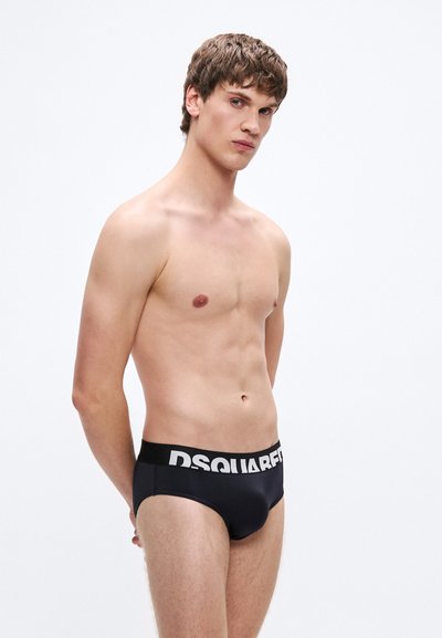 Μαύρα μαγιό σλιπ με λευκό, αντίθετο λογότυπο "DSQUARED" στη μέση. Το ύφασμα φαίνεται λείο με εφαρμοστή σχεδίαση.