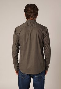 Bruin overhemd met knopen, versierd met kleine witte geometrische patronen, lange mouwen en een getailleerde pasvorm, gecombineerd met blauwe spijkerbroek.