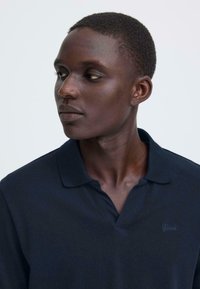 Polo bleu marine en tissu doux et texturé, doté d'un col à rabat et d'une broderie discrète "Blend" sur la poitrine.