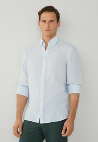 Camicia di lino azzurro chiaro con colletto button-down e maniche arrotolate; presenta un piccolo logo ricamato sul petto.
