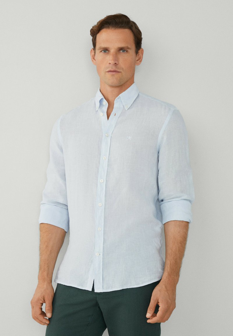 Camicia di lino azzurro chiaro con colletto button-down e maniche arrotolate; presenta un piccolo logo ricamato sul petto.