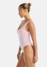 Světle růžové jednodílné plavky s kulatým výstřihem a širokými ramínky, vyrobené z hladké látky. Na boku je malý bílý logo.