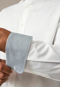 Hvid skjorte med en mønstret blå manchet. Manchetten har et geometrisk design med diamantformer. Skræddersyet pasform med en glat tekstur.