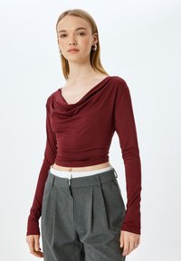 Bordeaux lange mouwen top met een gedrapeerde halslijn, gemaakt van rekbaar materiaal; gecombineerd met hoge taille grijze geplooide broek.