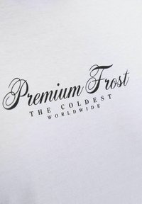 Balta medvilninė marškinėlių su juodu tekstu: "Premium Frost" ir "THE COLDEST WORLDWIDE." Paprastas, švarus dizainas su lygiu paviršiumi.