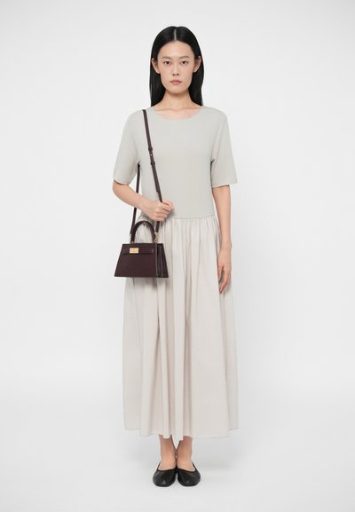 Svetle šedé šaty s krátkým rukávem a nařaseným pasem, v kombinaci s tmavě hnědou kabelkou se strukturovaným tvarem a zlatými kovovými prvky.