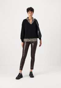 Czarny sweter z kołnierzem w leopardzi wzór, w zestawieniu z brązowymi spodniami z ekologicznej skóry i czarnymi butami na platformie. Prosty design, luźny krój.