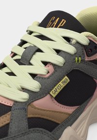 Gros plan sur une basket multicolore avec des lacets jaune pâle, des panneaux gris et roses, le logo "GAP" sur la languette et une étiquette "GAP EST. 1969" sur le côté.