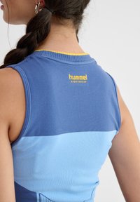 Niebieska sportowa koszulka bez rękawów z żółtym dekoltem. Posiada wzór w kolorach blokowych z ciemnoniebieskimi i jasnoniebieskimi sekcjami. Logo z tyłu.