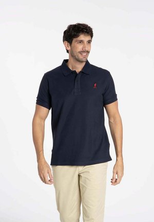 Polo en coton bleu marine avec un col, des manches courtes, et un logo rouge brodé sur la poitrine gauche. Ourlet plat et design simple.