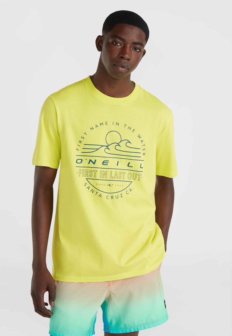 Camiseta de manga corta amarilla brillante con un diseño gráfico azul que presenta olas y un sol. Combinada con pantalones cortos de baño de degradado multicolor.
