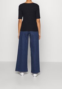 Černý, přiléhavý top s krátkými rukávy a stříbrnými horizontálními pruhy, kombinovaný s širokými modrými džíny a bílými teniskami.