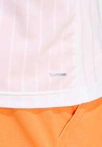 Chemise de sport blanche avec des rayures verticales rose clair, dotée d'un tissu perforé et du logo "CLIMACOOL", associée à un short orange texturé.
