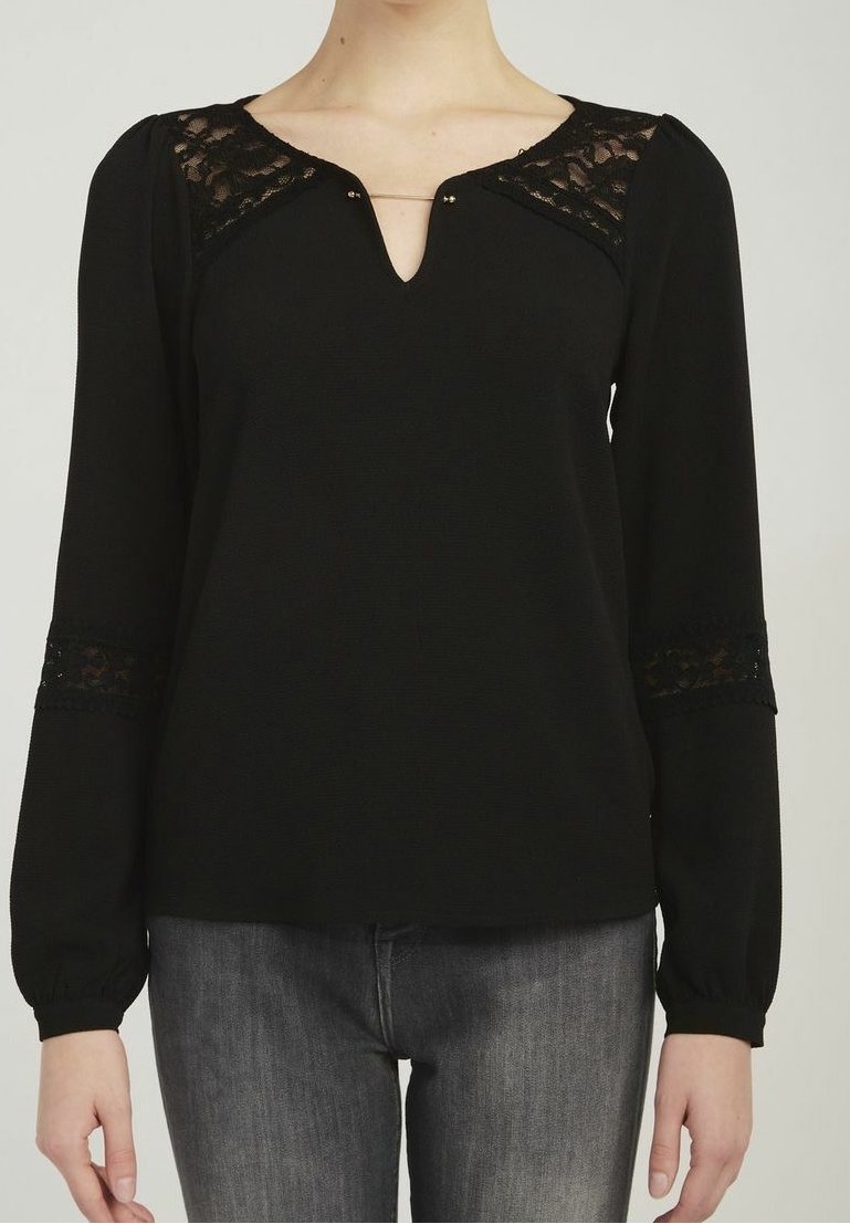 Svart långärmad topp med spetsdetaljer på axlarna och ärmsluten, en V-ringning med en dekorativ nål och en avslappnad passform.