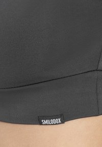Reggiseno sportivo nero con una texture liscia, design aderente e cuciture visibili. Presenta un piccolo etichetta con "SMILODOX" sul lato.