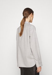 Hellgraues Langarmshirt mit kragenähnlichem Ausschnitt, lockerer Passform und knöpfbaren Manschetten. Glatte Textur mit einem subtilen gewebten Muster.