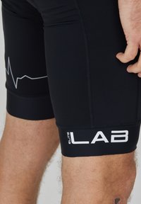 Schwarze Triathlon-Shorts aus dehnbarem Material, mit einem Herzschlaglinien-Design und großem "ELITE LAB"-Logo am Bein, enganliegend.