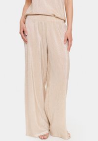 Beige, wide-leg pants with a ribbed texture and subtle shimmer. Elastic waistband and loose fit, enhancing comfort and flow.