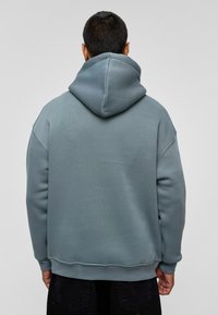 Hoodie van zachte, gedempte blauwe stof. Heeft een relaxed fit, een gestructureerd oppervlak en een eenvoudig ontwerp zonder zichtbare logo's of patronen.