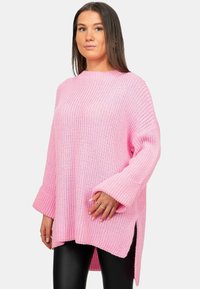 Overmaatse roze gebreide trui met ribbelstructuur, lange mouwen, zijsplitten en een ronde halslijn, gecombineerd met zwarte leggings.