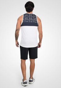 Débardeur blanc avec une partie supérieure à motif marine, associé à un short noir. Le débardeur a un ourlet arrondi et une coupe décontractée.