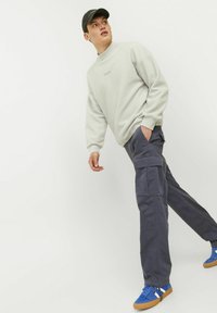 Lys grå sweatshirt med høj krave, parret med mørkegrå cargo-bukser med flere lommer. Blå sneakers fuldender antrekket.