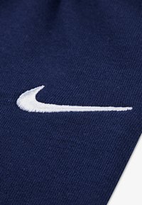 Marineblått stoff med et teksturert mønster, med en hvit brodert Nike Swoosh på den ene siden.